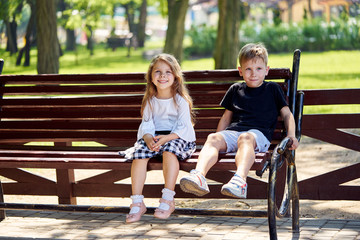 A boy and a girl are sitting in a park on a bench and smiling.