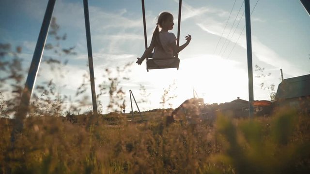 Happy little girl have fun sway spin on a swing on nature sunset. A silhouette young girl swings on a swing.