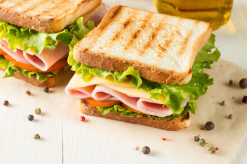 Close-up photo of a club sandwich. Sandwich with meat, prosciutto, salami, salad, vegetables, lettuce, tomato, onion and mustard on a fresh sliced rye bread on wooden background. Olives background.