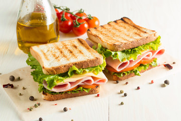 Close-up photo of a club sandwich. Sandwich with meat, prosciutto, salami, salad, vegetables, lettuce, tomato, onion and mustard on a fresh sliced rye bread on wooden background. Olives background.