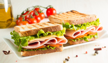 Close-up photo of a club sandwich. Sandwich with meat, prosciutto, salami, salad, vegetables, lettuce, tomato, onion and mustard on a fresh sliced rye bread on wooden background. Olives background.