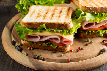 Close-up photo of a club sandwich. Sandwich with meat, prosciutto, salami, salad, vegetables, lettuce, tomato, onion and mustard on a fresh sliced rye bread on wooden background. Olives background.