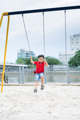 Happy asian boy swinging at the playground in the park