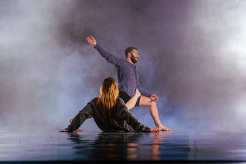 Shoeless dance couple performing multiple unique dance moves in front of a black background surrounded by a lot of smoke.