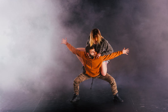 Strong male dancer and an elegant female dancer perform an exotic and unique dance moves in front of a black background while wearing urban clothes. © qunica.com