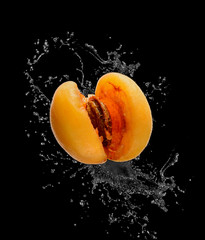 Naklejka na ściany i meble Broken apricot with bone on black background. From it scatter splashes.