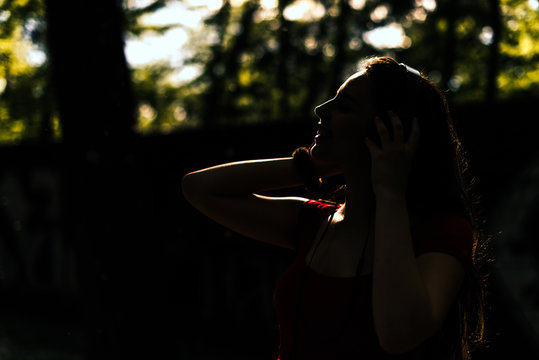 Silhouette girl is listening to music on her headphones, low key, dark image