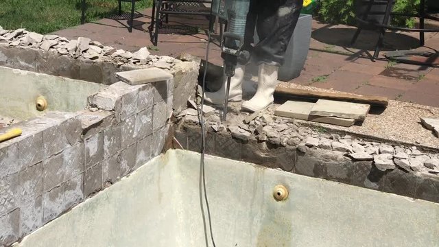 Construction worker demolishing coping, tile and concrete around empty swimming pool and hot tub for remodel