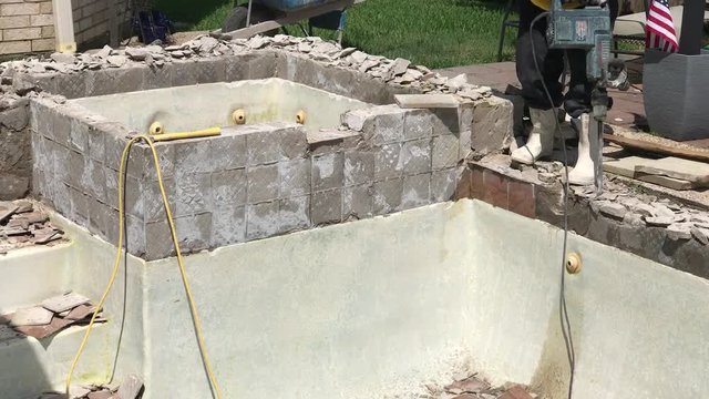 Construction worker demolishing coping, tile and concrete around empty swimming pool and hot tub for remodel