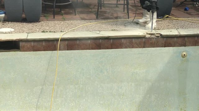 Construction worker demolishing coping, tile and concrete around empty swimming pool and hot tub for remodel