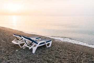 Fototapeta na wymiar Two plastic sun beds on the sea beach at sunrise. Summer vacation concept.