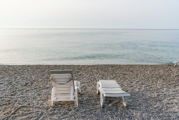 Two plastic sun beds on the sea beach at sunrise. Summer vacation concept. Back view.