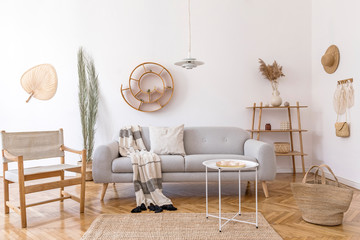 Stylish and cozy interior of living room with elegant rattan accessories, design armchair, gray sofa and wooden shelf. Korean style of home decor. Hanging rattan snail with airplants. 
