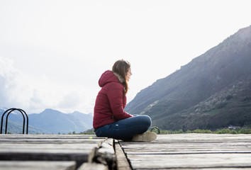 Fototapeta na wymiar Alone women relax on wooden dock at peaceful lake. Girl meditation with red jacket in a wood pier