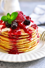 Stack of homemade delicious vanilla pancakes topped with sour cream,rasbberry syrup and berries.
