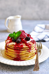 Stack of homemade delicious vanilla pancakes topped with sour cream,rasbberry syrup and berries.