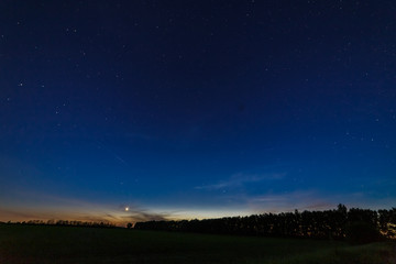 Starry sky after sunset over the field and trees. Planet Venus is above the horizon.