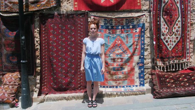 Beautiful tourist girl posing on street in front of old east oriental carpets.