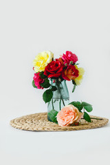 Coloful roses in vase on a wicker napkin on white background