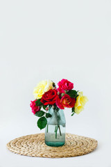 composition of colorful roses in a vase on a wicker napkin on a white background