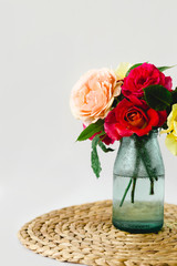 Coloful roses in vase on a wicker napkin on white background