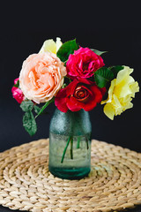 Coloful roses in vase on a wicker napkin on black background