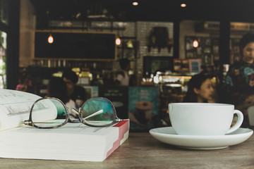 Eyes glasses on book with cup of coffee on wooden desk in blur background.