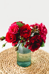 Coloful roses in vase on a wicker napkin on white background