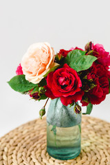 Coloful roses in vase on a wicker napkin on white background