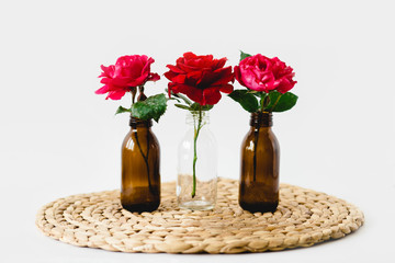 Red roses in glass vases on a wicker napkin on white background