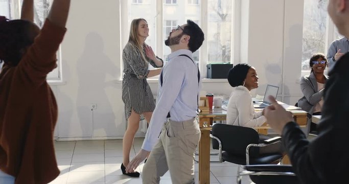 Fun young successful businessman sharing big career success celebration with coworkers doing crazy dance walk at office.