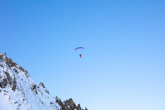 A parapente or paraglider is flying high above the snow capped mountains