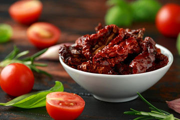 Sun dried tomatoes in white bowl with fresh herbs and spices on wooden table