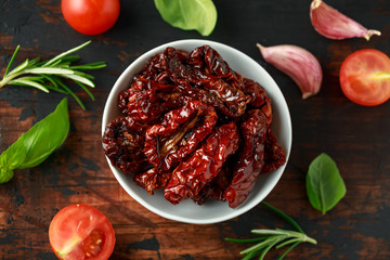 Sun dried tomatoes in white bowl with fresh herbs and spices on wooden table
