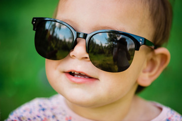 Baby with sunglasses on the green grass background on a sunny day, lifestyle