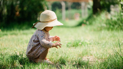 baby girl seating on the grass - summer day of childhood, straw hat, copy space