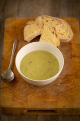 Fresh leek and potato soup in a bowl on a wooden board with crusty white bread and butter