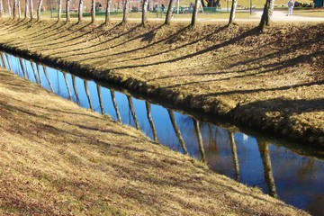 The straightened Glan creek in Salzburg city, in February. Tree stems mirror in the water. Salzburg, district Lehen, Austria, Europe.