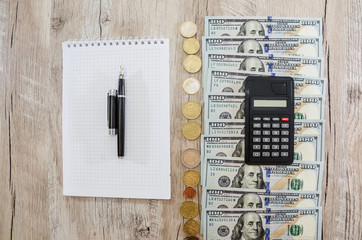 calculator, notebook, dollars and coins. Hundred dollar bills and coins in a row on the table. View...