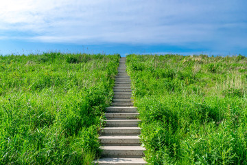 A stone staircase rises in the blue sky. The concept of career growth or the road to heaven. Steps on a high hill lead to the sky.