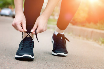 Morning running. Young lady running on a rural road during sunset in black sneakers. Girl tying shoelaces before running