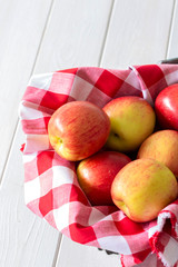 Apples, Jazz variety, on gingham cloth in a wicker trug basket.  On a white wood background.