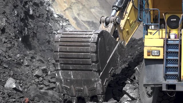 an excavator digs a hole in a coal mine and pours it into a dump truck