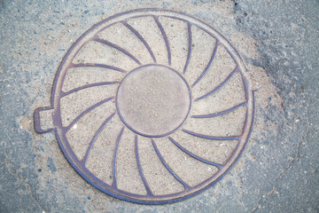 Manhole cast iron heavy lilac with a pattern of divergent rays on the background of green grass.