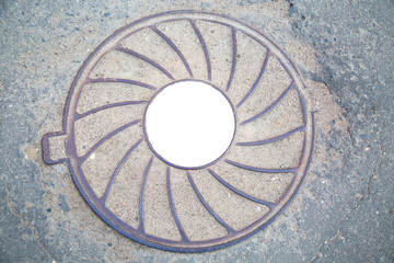 Manhole cast iron heavy lilac with a pattern of divergent rays on the background of gray asphalt. In the center of the round white background for photo inscription