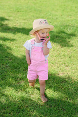 Smiling girl wearing pink sunglasses and walks on green lawn. The concept of summer vacation and carefree childhood.