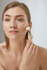Beauty skin care. Woman using jade roller for face massage © puhhha
