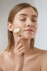 Beauty skin care. Woman using jade roller for face massage