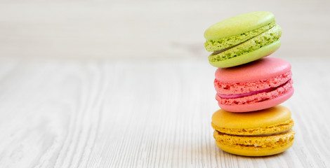 Stack of colorful macarons on a white wooden surface, side view. Space for text.
