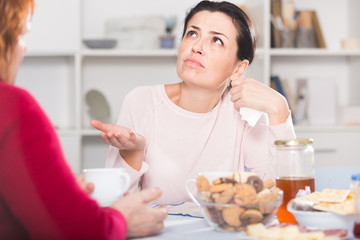 Portrait of sad female talking with mother at table